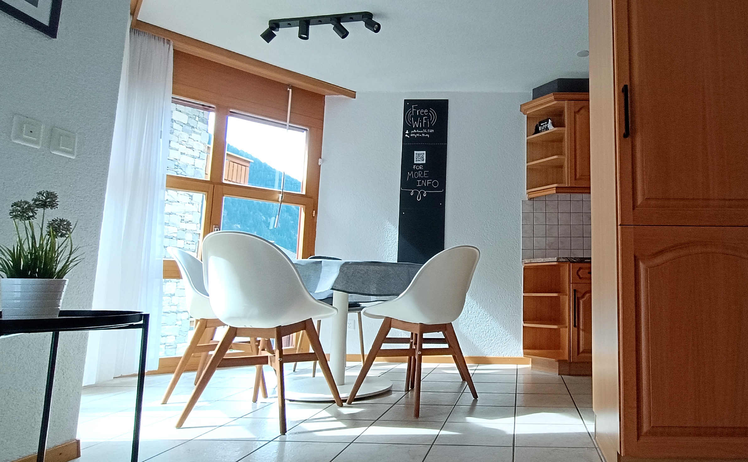 Zona pranzo luminosa dell'appartamento Altrove a Leukerbad, con scorcio della cucina e lavagna informativa Free WiFi